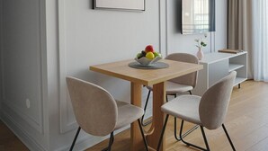 A modern dining area with a wooden table, two chairs, a fruit bowl, a pendant light, a flat-screen TV, and a vase with flowers. - Madera (Čačak)