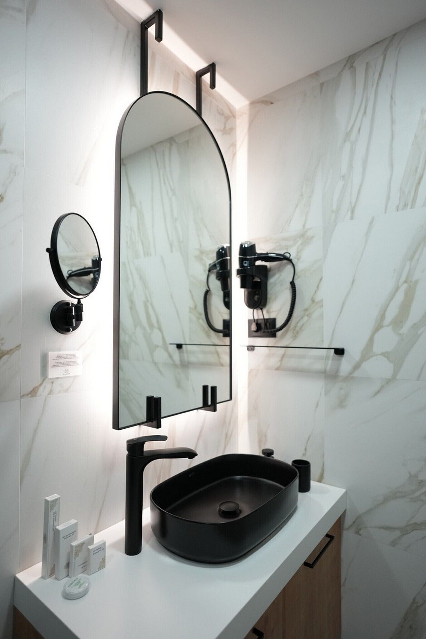 A modern bathroom with a black sink, a large mirror, and marble walls.