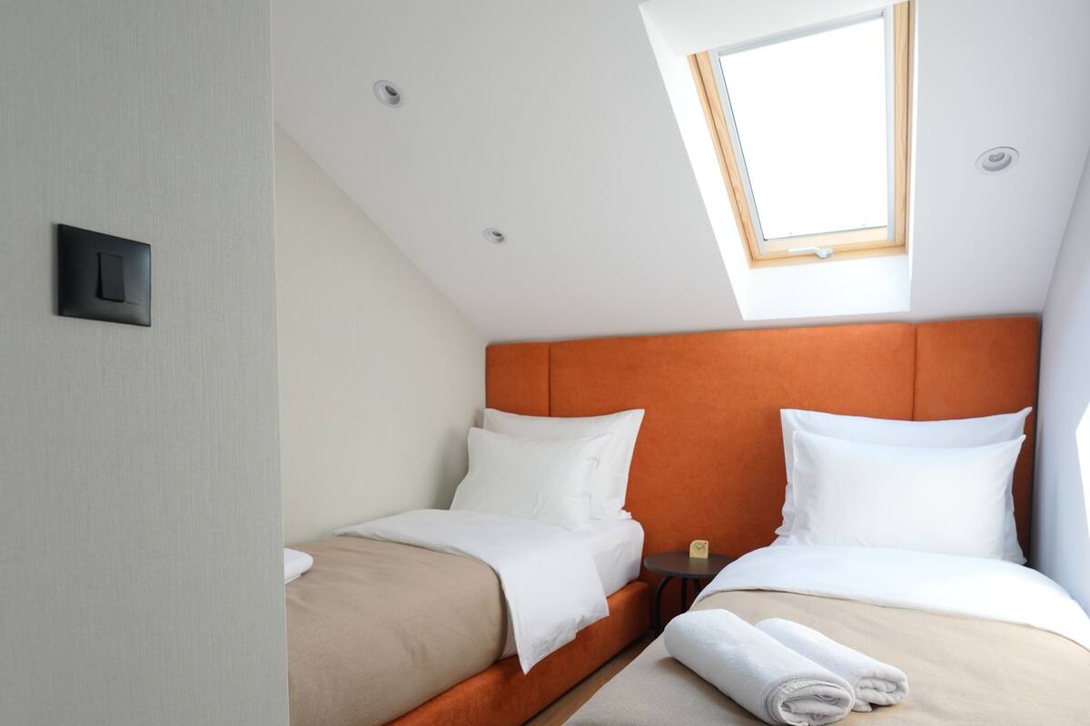 Habitación de hotel con dos camas, un tragaluz y una pequeña mesa.