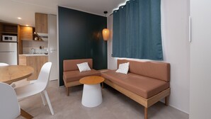 Een moderne woonkamer met een bank, een rond bijzettafeltje, een eettafel met stoelen, en een keukenhoek met een magnetron.
