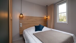 Een slaapkamer met een houten hoofdeinde, een bed met wit beddengoed, een beige plaid en twee hanglampen.