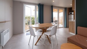 Een moderne woonkamer met een ronde houten tafel, witte stoelen, een bruine bank en een keukenhoek met een magnetron.