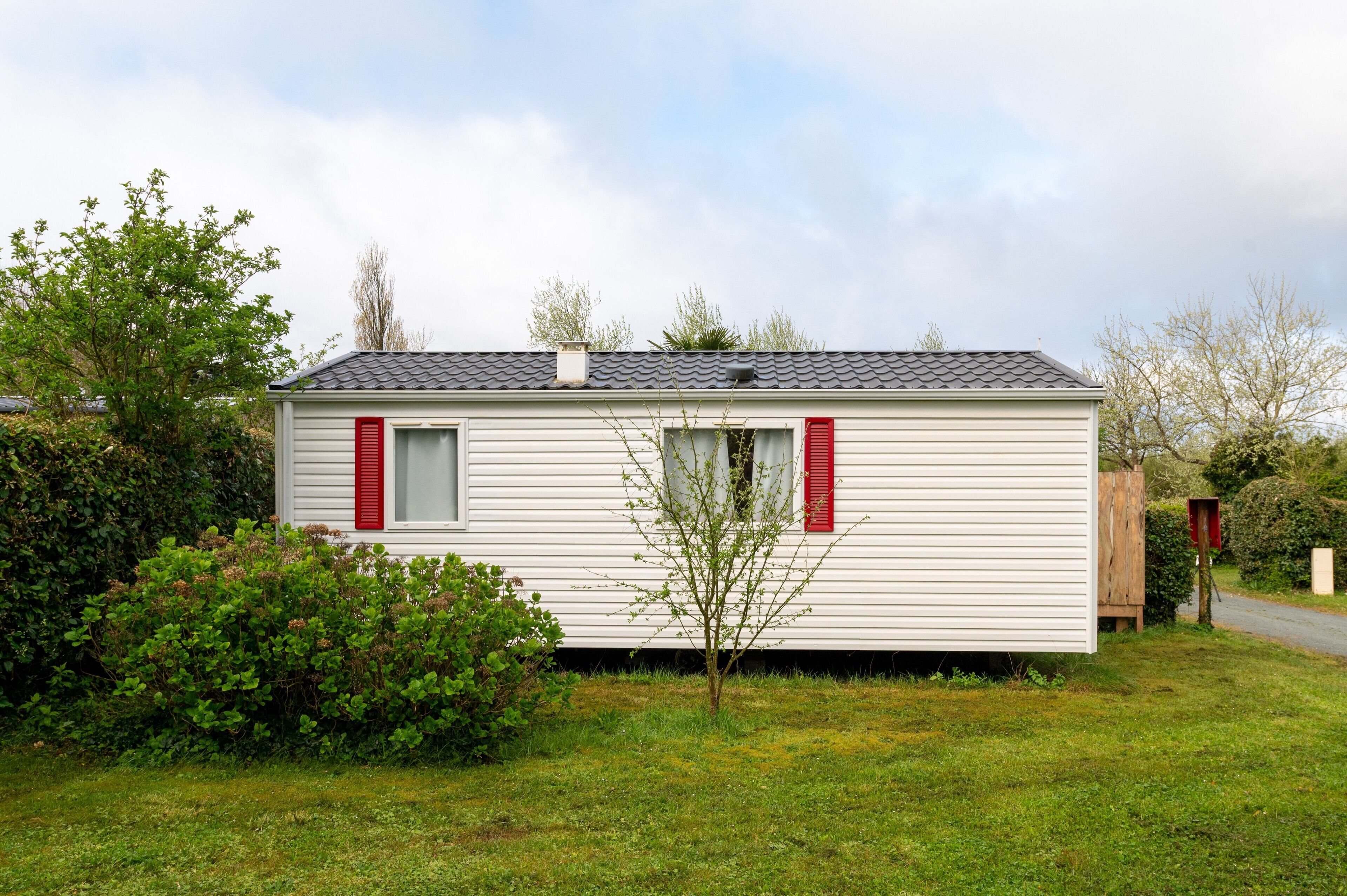 A single-story mobile home with a sloped roof, white siding, and red shutters.