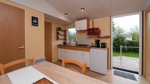 A compact kitchen with a dining table, chairs, a microwave, and a small refrigerator. - Mobile Home “Les Volets rouges” with Private Terrace (Plouhinec)