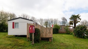 A small, single-story mobile home with a red mailbox and a wooden fence. - Mobile Home “Les Volets rouges” with Private Terrace (Plouhinec)