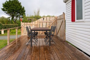 Une terrasse en bois avec une table et des chaises, une clôture en bois et un bâtiment blanc avec des volets rouges.