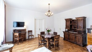 A dining area with a wooden table, chairs, a chandelier, and a television on the wall.