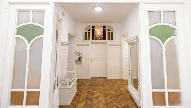 A hallway with a wooden herringbone floor, white doors, and a stained glass window.