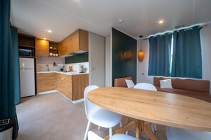 Une cuisine moderne avec des meubles en bois, un coin repas avec une table en bois et des chaises blanches, et un espace détente avec un banc et des coussins.