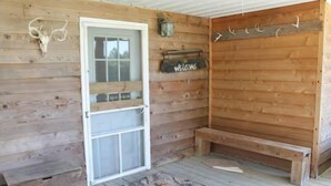 Uma cabana de madeira com porta, placa de boas-vindas, um banco e um crânio de animal montado na parede.