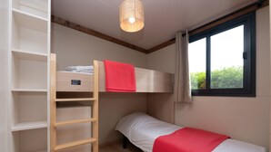 Uma cama beliche com um cobertor vermelho, uma escada de madeira e uma janela com cortinas.