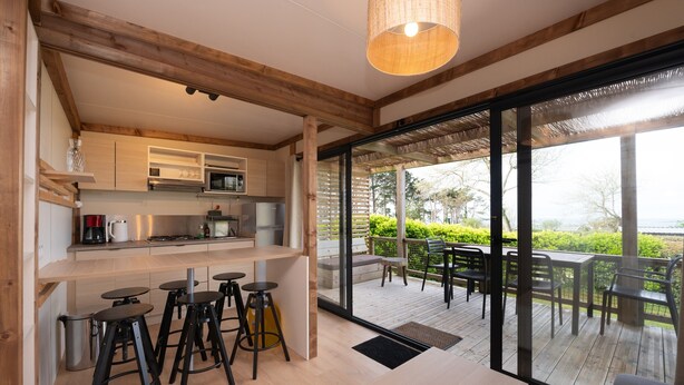 Uma cozinha moderna com banquetas, uma sala de jantar com mesa e cadeiras, e vista para o exterior.