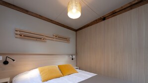 A bedroom with a bed, bedside tables, a wall-mounted shelf, a hanging light fixture, and a wooden ceiling beam. - Chalet "35 m² - Molène" in Plouhinec, 5 Guests, 2 Bedrooms (Plouhinec)
