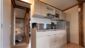 A compact kitchen with wooden cabinets, a built-in microwave, and a refrigerator. - Chalet "35 m² - Molène" in Plouhinec, 5 Guests, 2 Bedrooms (Plouhinec)