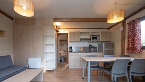 A modern kitchen with white cabinets, a dining table with chairs, and a built-in microwave. - Chalet "35 m² - Molène" in Plouhinec, 5 Guests, 2 Bedrooms (Plouhinec)