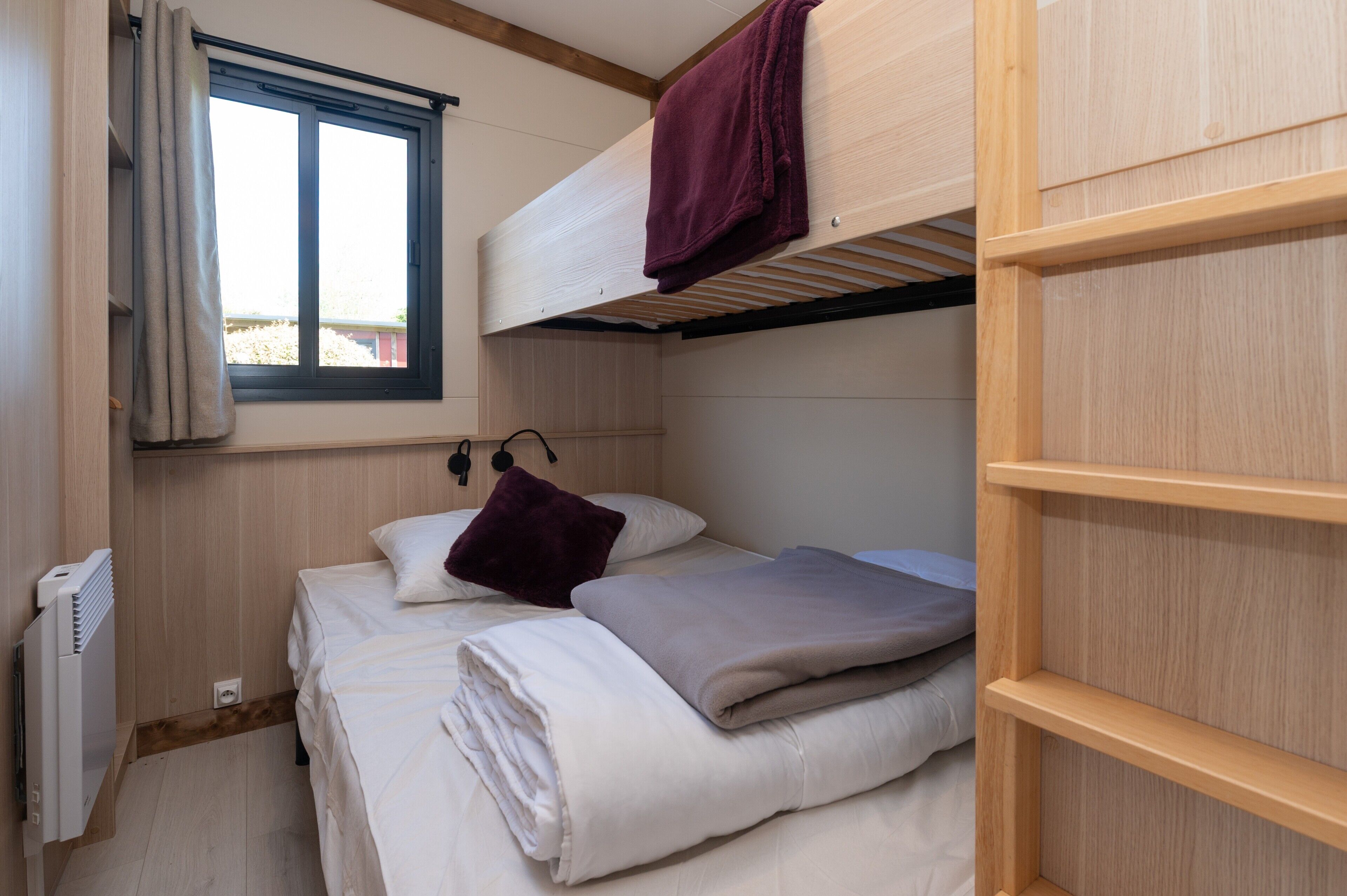 A bunk bed with a window, a radiator, and a wooden shelf.