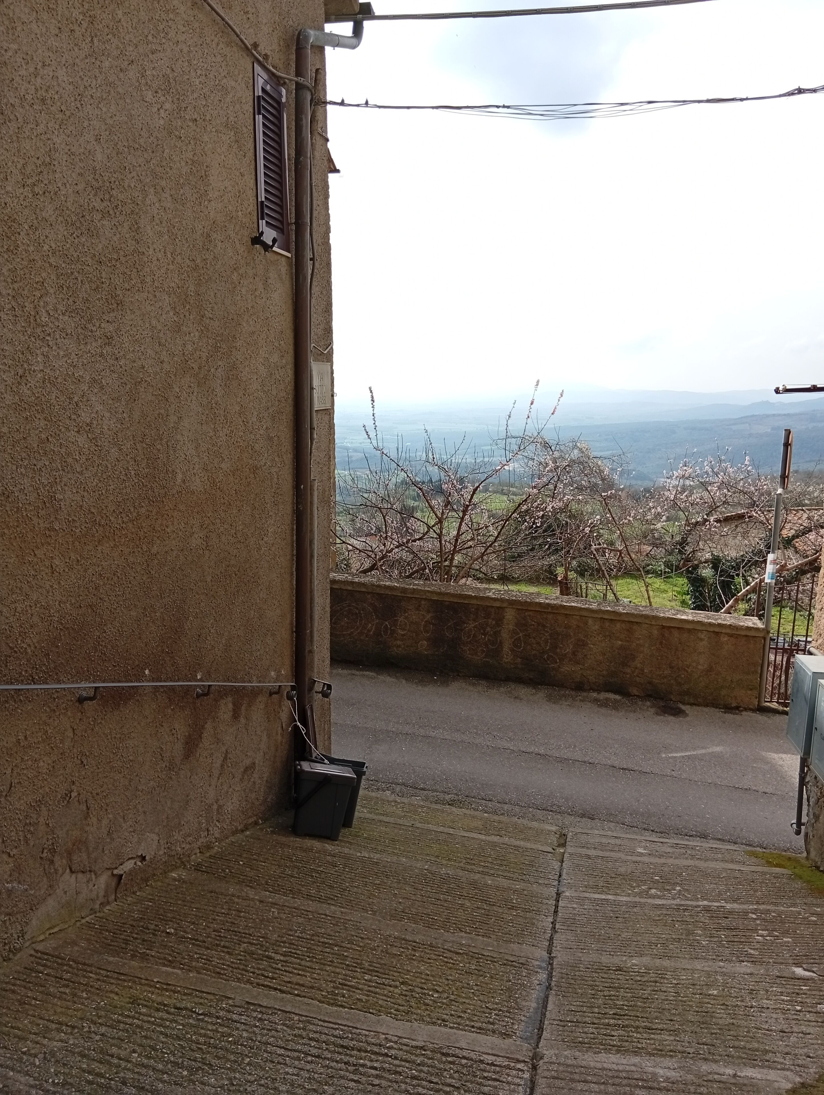 Un edificio in cemento con una porta in metallo, una finestra con sbarre metalliche e una vista su un paesaggio con alberi e un orizzonte lontano.