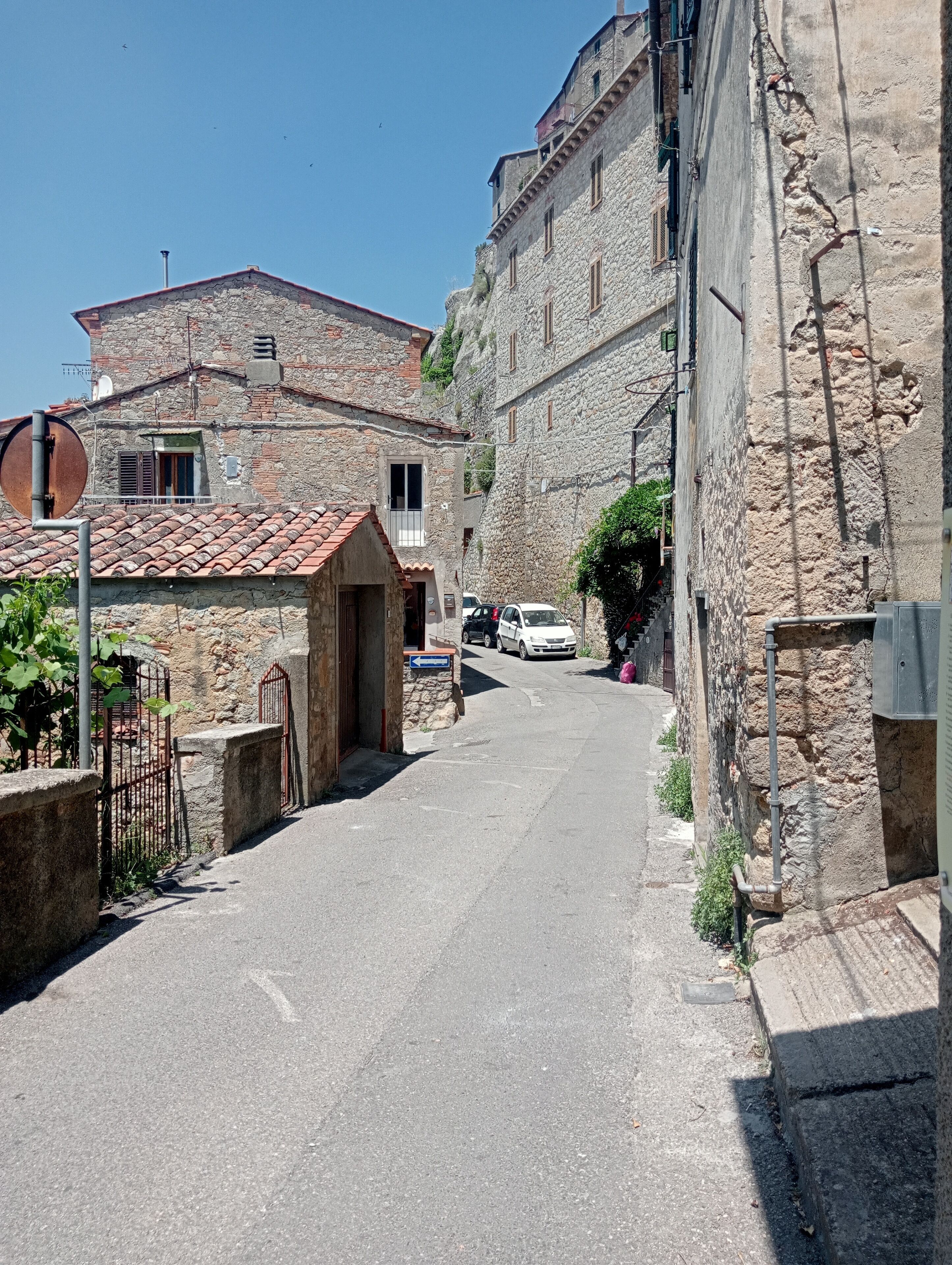 Une rue étroite bordée d’immeubles en pierre à l’architecture traditionnelle, avec une petite porte et une voiture garée.