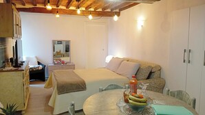 Une pièce confortable avec un lit, une table avec des fruits, une chaise, un bureau avec un ordinateur et un miroir.