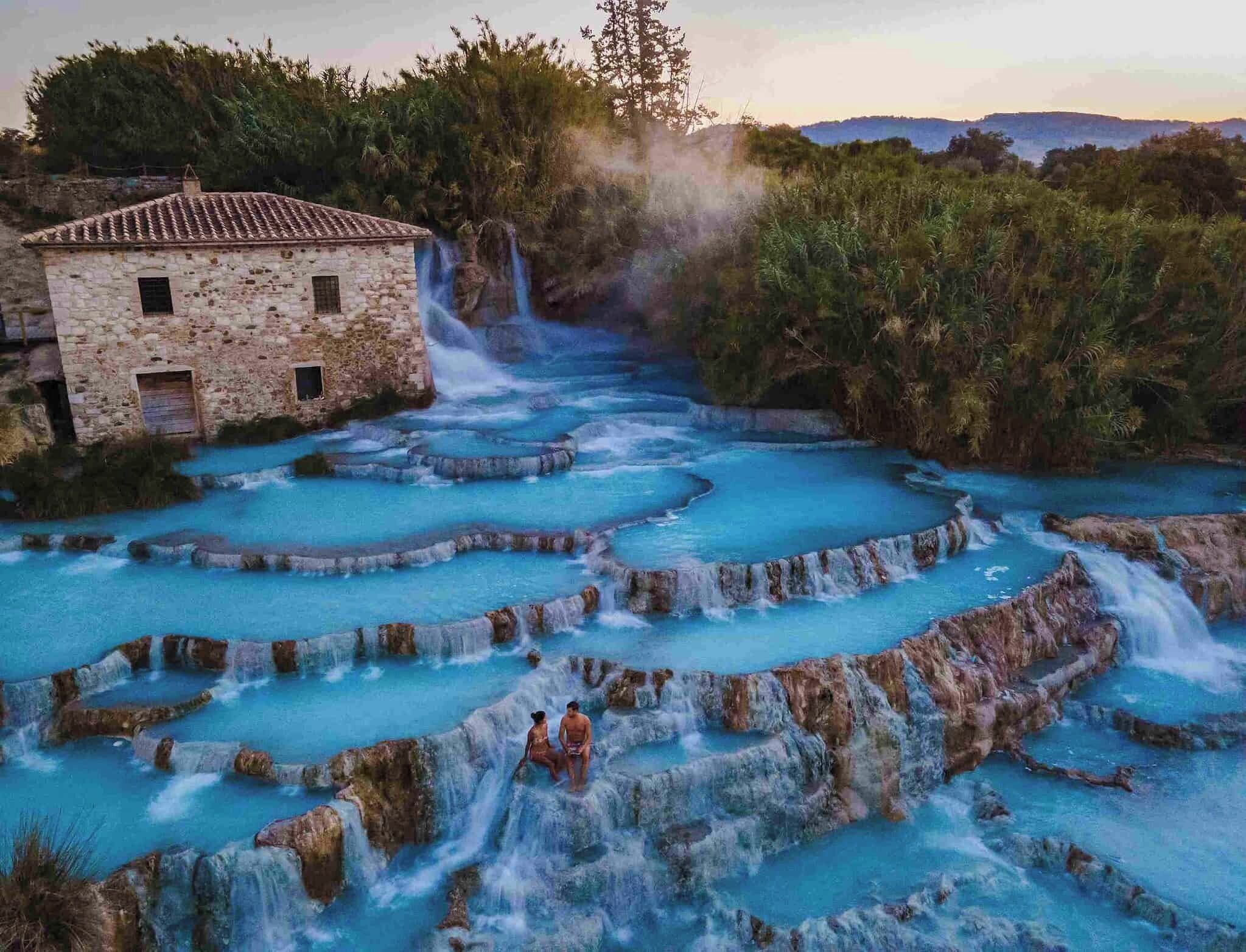 A stone building with a tiled roof, terraced pools of water, and a waterfall.
