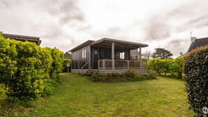Een laag gebouw met een veranda, omgeven door keurig onderhouden hagen en een gazon.
