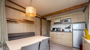 Een kleine keuken met een eethoek, houten balken, een hangende lamp, een ingebouwde magnetron en een koelkast.