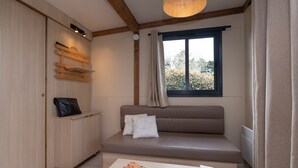 A room with a sofa, a small table, a cabinet, a window with curtains, and a ceiling light fixture. - Chalet “20m² - Les Îles Vierges” with Terrace (Plouhinec)