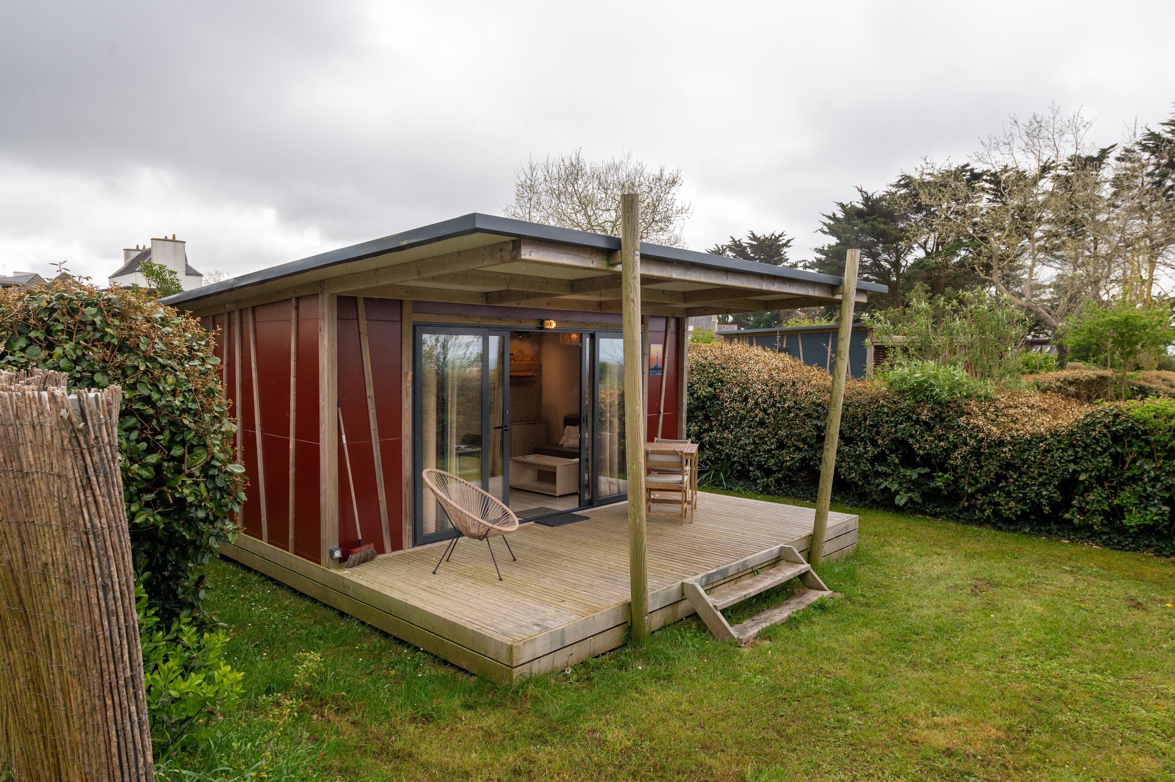A modern house with a deck, a glass door entrance, and a chair outside.