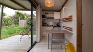 A modern kitchen with wooden cabinets, a dining table, and a chair. - Chalet “20m² - Les Îles Vierges” with Terrace (Plouhinec)