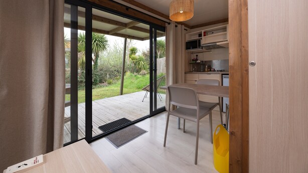 A modern kitchen with a dining area, large sliding glass doors leading to an outdoor deck, and a wooden ceiling. - Chalet “20m² - Les Îles Vierges” with Terrace (Plouhinec)