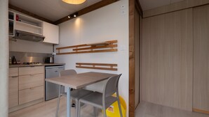 A modern kitchen with a wooden table and chairs, a built-in stove, and a yellow trash bin. - Chalet “20m² - Les Îles Vierges” with Terrace (Plouhinec)