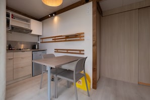 Une cuisine moderne avec une table et des chaises en bois, une cuisinière encastrée et une poubelle jaune.