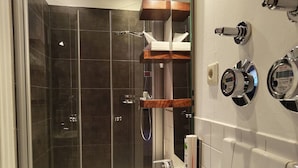 Un bagno moderno con doccia vetro, lavabo bianco, mobile bagno in legno e specchio con bilancia integrata.