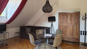 Una stanza accogliente con un tavolo rotondo, sedie in vimini, un divano scuro, un televisore e un'ampia armadiatura in legno.