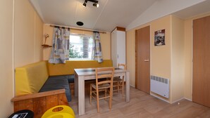 Une pièce avec un canapé jaune, une table à manger en bois avec des chaises, une fenêtre avec des rideaux, un radiateur et une porte.