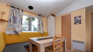 Une pièce avec une table en bois, un canapé jaune, une fenêtre avec des rideaux, une porte et une affiche accrochée au mur.
