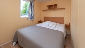 Une chambre à coucher avec un lit, une fenêtre avec des rideaux, une tête de lit en bois et une étagère au-dessus du lit.