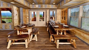 Un comedor rústico de madera con bancos y mesas, ventanas amplias con persianas y vistas al exterior.