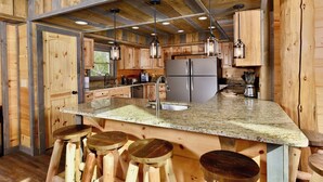 Una cocina con armarios de madera, encimera de granito, electrodomésticos de acero inoxidable y taburetes de bar.
