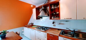 A kitchen with white cabinets, a gas stove, a sink, and a wooden table. - Room "A Splendid Room in Wonderful Rome" with Private Terrace, Wi-Fi, and Air Conditioning (Roma)