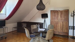 Un comedor con una mesa redonda, sillas de mimbre, una lámpara negra y un televisor sobre un carrito.