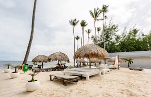 Een strandlounge met rieten parasols, ligstoelen en plantenpotten.