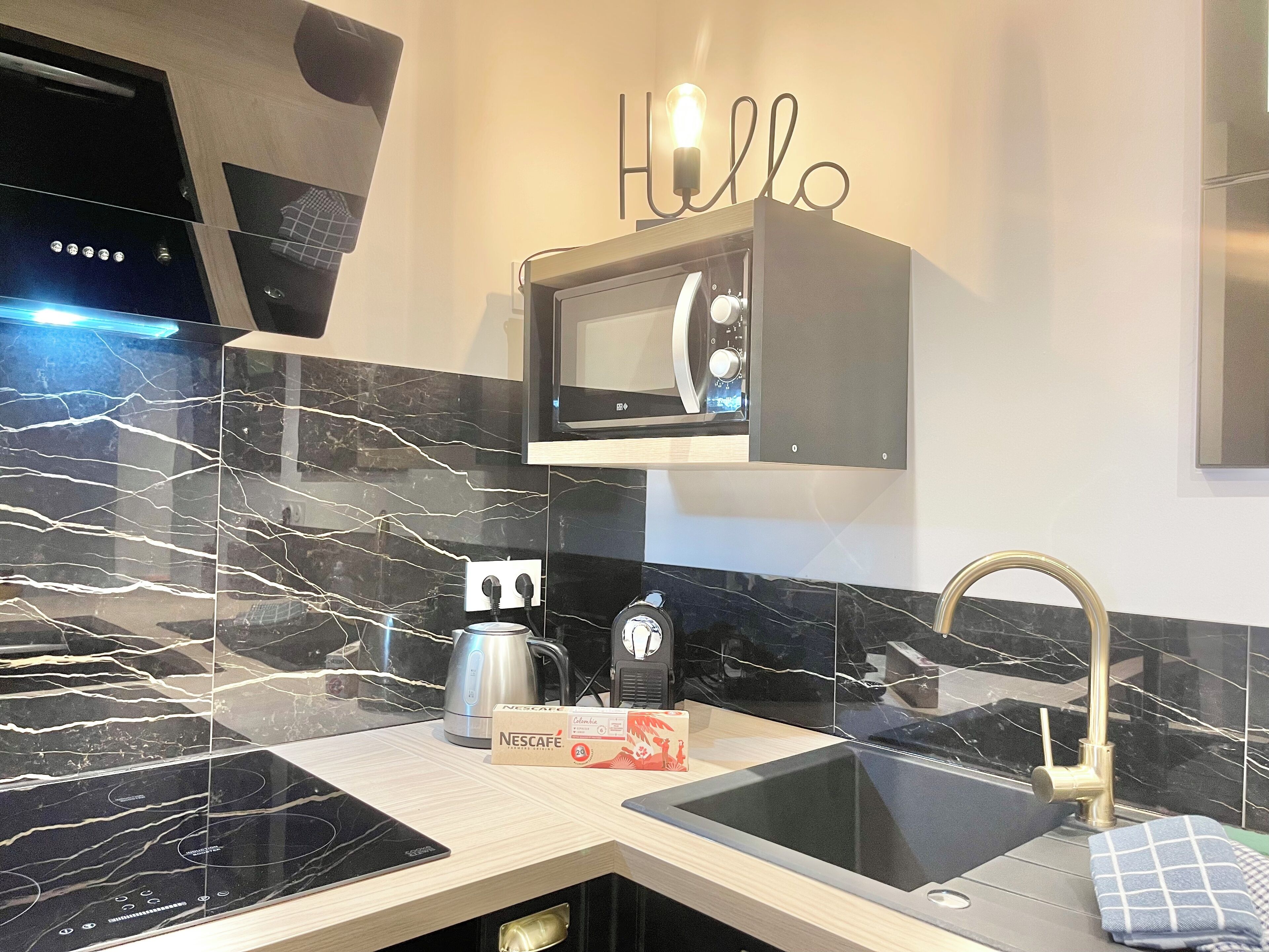 Uma cozinha moderna com painel de fundo de mármore preto, micro-ondas embutido, cafeteira e pia com torneira dourada.