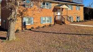 A two-story brick house with a front porch, a garage, and a tree in the foreground. - Crewe Corner <br>Apartment C (Crewe)