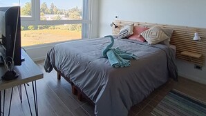 A bedroom with a bed, a desk with a computer, a window with a view of trees and buildings, and a ceiling light fixture. - Kasa and family 809 (Valdivia)