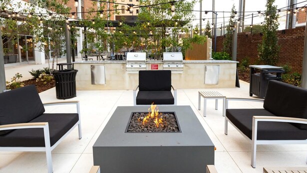 An outdoor patio with a central fire pit, surrounded by black cushioned chairs and a small table. - Landing | Chic 1BD, Game Room, Courtyard (Birmingham)