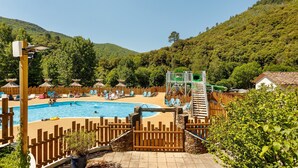 Una piscina amb terrassa de fusta, tobogan i zona delimitada amb gandules.