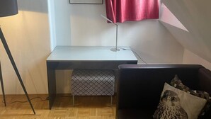 Una habitación con escritorio, silla, lámpara de pie, sofá y cortina roja.