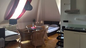Una habitación compacta con cama, una mesa de comedor con sillas, una kitchenette y un televisor.