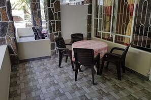 A patio area with a round table and six chairs, stone walls, and a window with curtains. - Pereybere Beach Apartments: Superior Apartment (Pereybere)